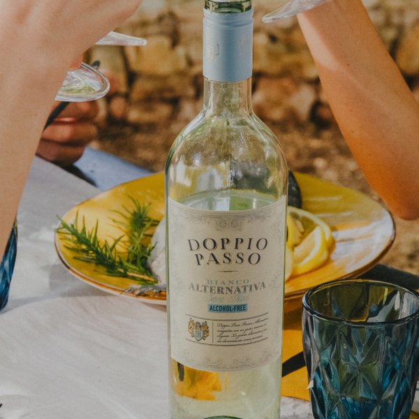 Eine lebhafte Outdoor-Dining-Szene mit Freunden, die mit Gläsern anstoßen, umgeben von bunten Tellern und einer Flasche Doppio Passo-Wein.